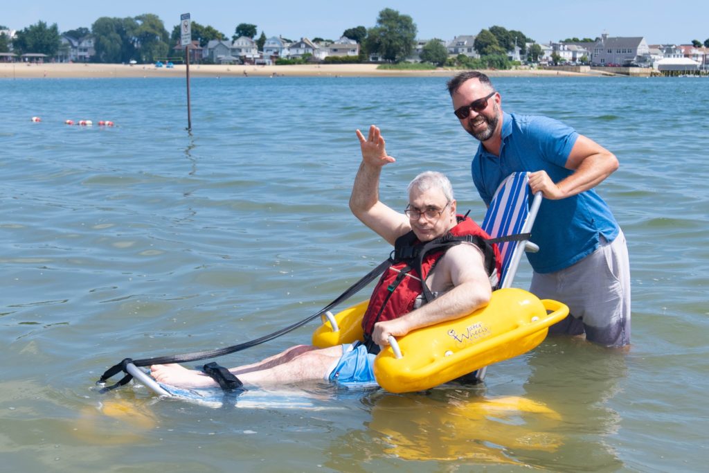 Chief Program Officer Drew Warren enjoys the water with a Triangle resident in a beach wheelchair.