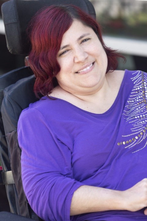 Michelle Garcia, Co-Founder, The National Coalition for Latinx with Disabilities, is smiling in a wheelchair. She has red hair and is in a purple shirt.