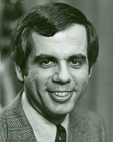 A black and white official congressional portrait of Tony Coelho from the shoulders up smiling for the camera wearing a black tie, medium toned shirt, and checked blazer. 